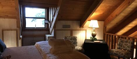 A cozy attic bedroom with a bed, a chair, a lamp, and a window.