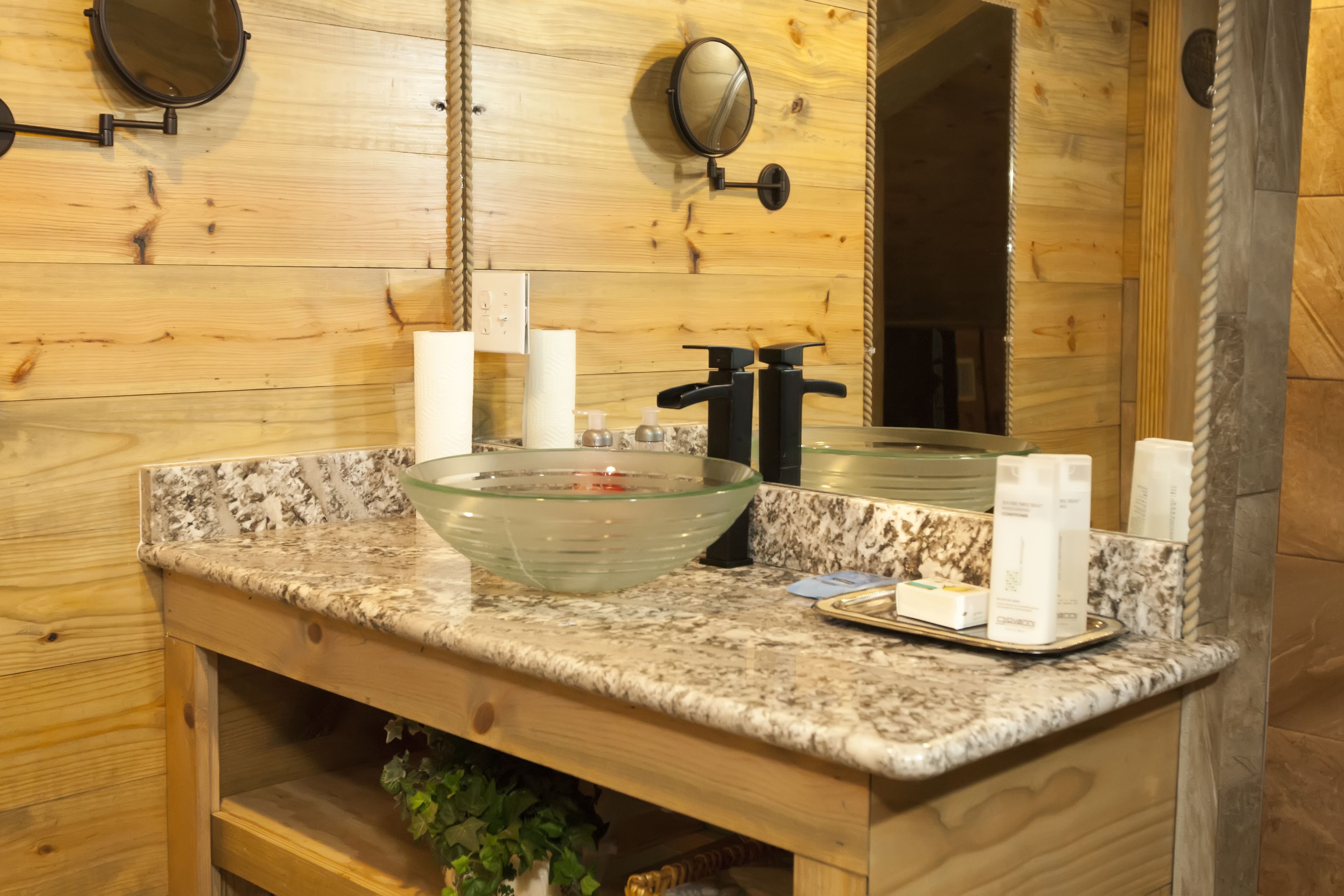 Un bagno con parete in legno, un lavabo in vetro, uno specchio e articoli da toilette.