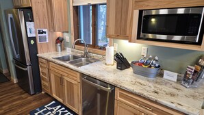 A modern kitchen with wooden cabinets, stainless steel appliances, a double sink, and a granite countertop. - Lakeside Escape/ Ski Nordic Mt./ lakefront cabin/ pontoon rental/ Pets/ Hot Tub! (Wautoma)