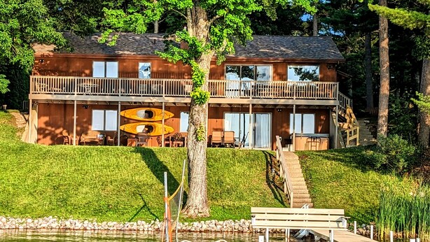 A cabin with a dock, a boat, and a staircase leading to a balcony. - Lakeside Escape/ Ski Nordic Mt./ lakefront cabin/ pontoon rental/ Pets/ Hot Tub! (Wautoma)