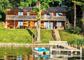 A cabin with a dock, a boat, and a staircase leading to a balcony.