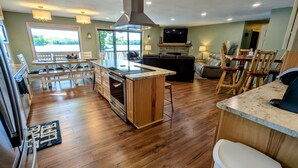 A spacious kitchen with wooden flooring, a central island, and a large stove. There is a dining area with a table and chairs, and a living room with a sofa and a TV. - Lakeside Escape/ Ski Nordic Mt./ lakefront cabin/ pontoon rental/ Pets/ Hot Tub! (Wautoma)
