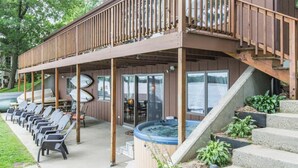 A covered outdoor area with lounge chairs, a hot tub, and a deck with a railing. - Lakeside Escape/ Ski Nordic Mt./ lakefront cabin/ pontoon rental/ Pets/ Hot Tub! (Wautoma)