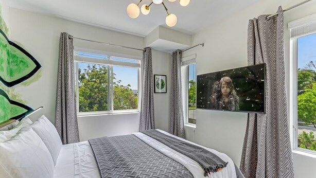 Un dormitorio con cama, televisor y ventana con cortinas.