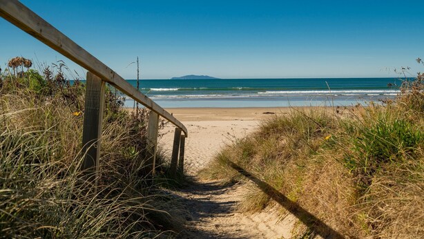 Ein Strandweg, der zum Meer führt, mit einem Holgitter links.