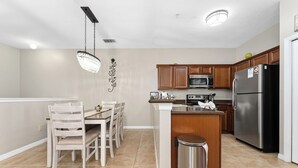 A modern kitchen with wooden cabinets, a stainless steel refrigerator, and a dining area with a chandelier. - Family Friendly 2BR Condo at Oakwater Resort – 1.5 Miles to Disney (Kissimmee)