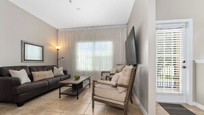 A living room with a brown sofa, a beige armchair, a coffee table, and a TV. - Family Friendly 2BR Condo at Oakwater Resort – 1.5 Miles to Disney (Kissimmee)