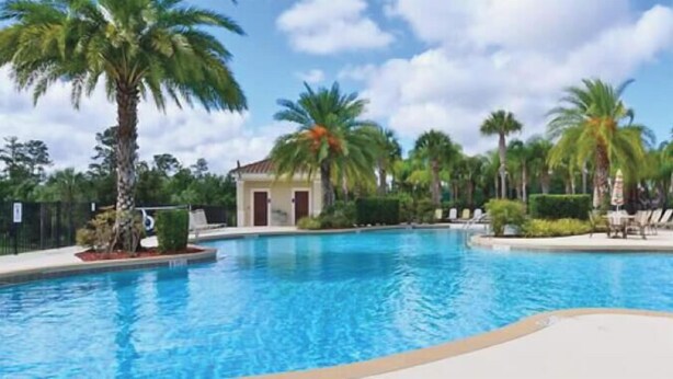 A swimming pool surrounded by palm trees and a building with a tiled roof. - Family Friendly 2BR Condo at Oakwater Resort – 1.5 Miles to Disney (Kissimmee)