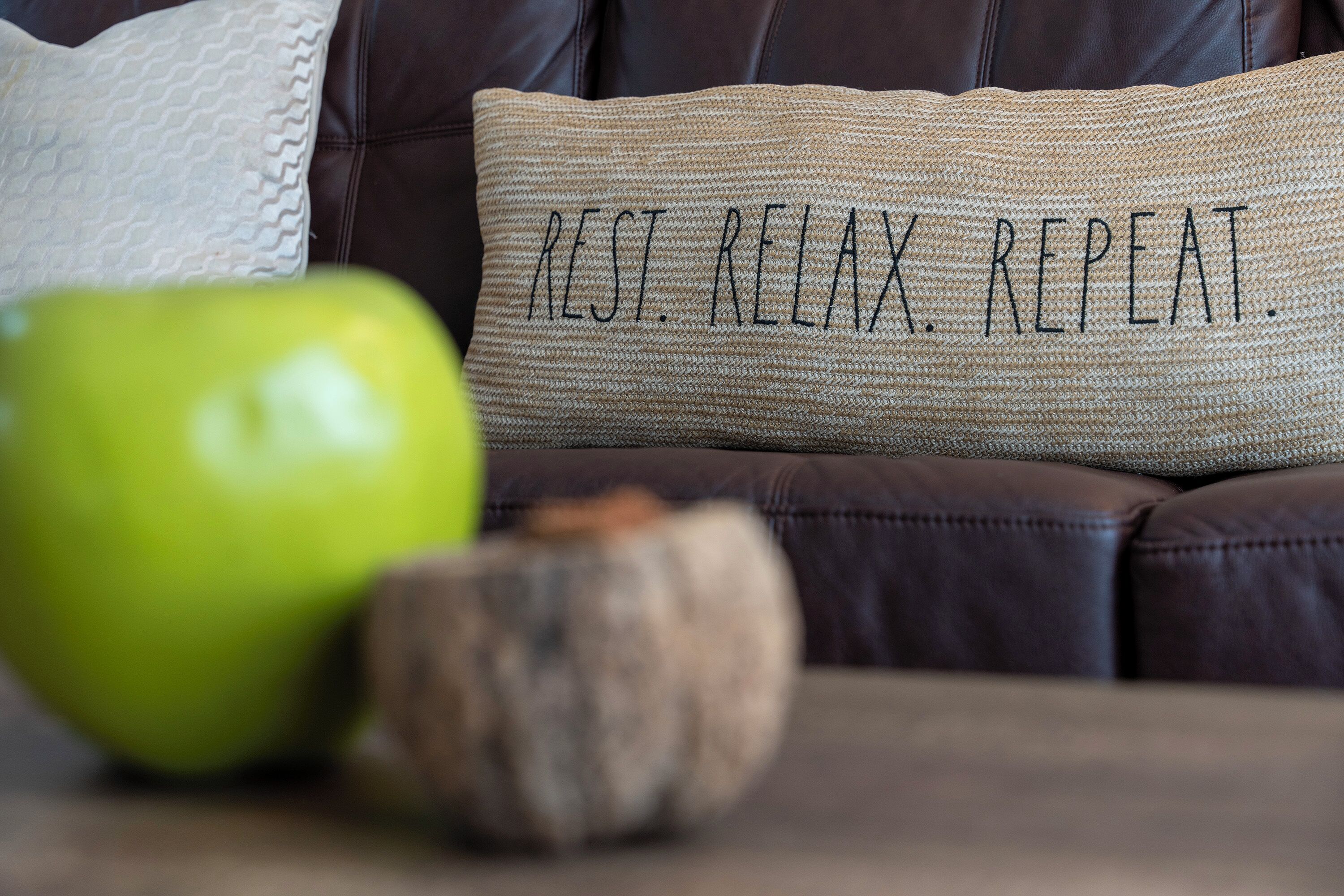 A brown leather couch with a pillow that reads "REST. RELAX. REPEAT."