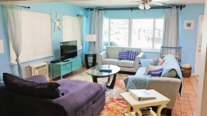 Ein Wohnzimmer mit Sofa, Sessel, Couchtisch, Fernseher und Deckenventilator.
