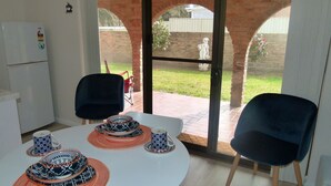 Ein Essbereich mit einem runden Tisch, zwei Stühlen und Blick auf eine Ziegelwand und einen Garten durch große Fenster.