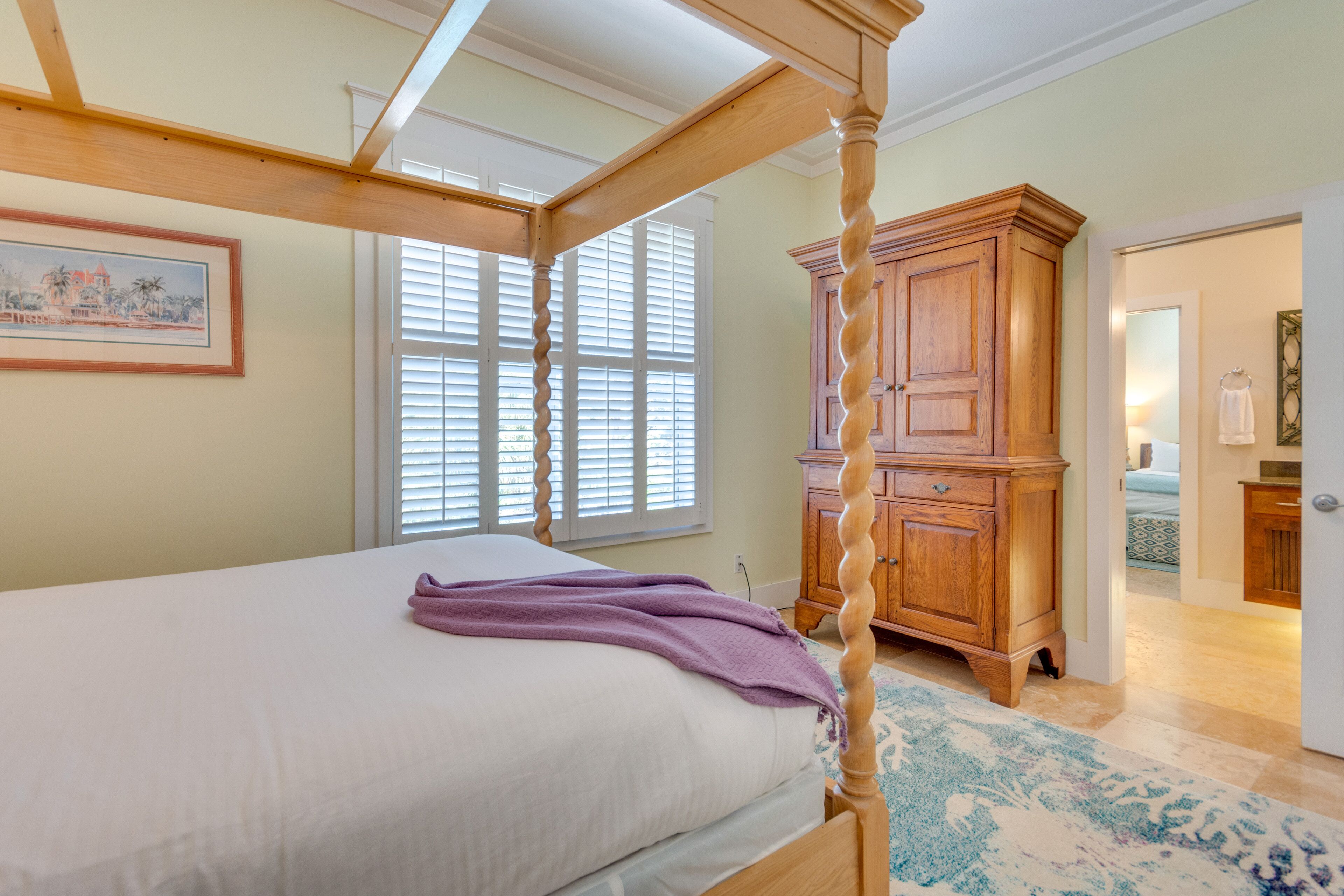 A bedroom with a four-poster bed, a wooden wardrobe, and a painting on the wall.