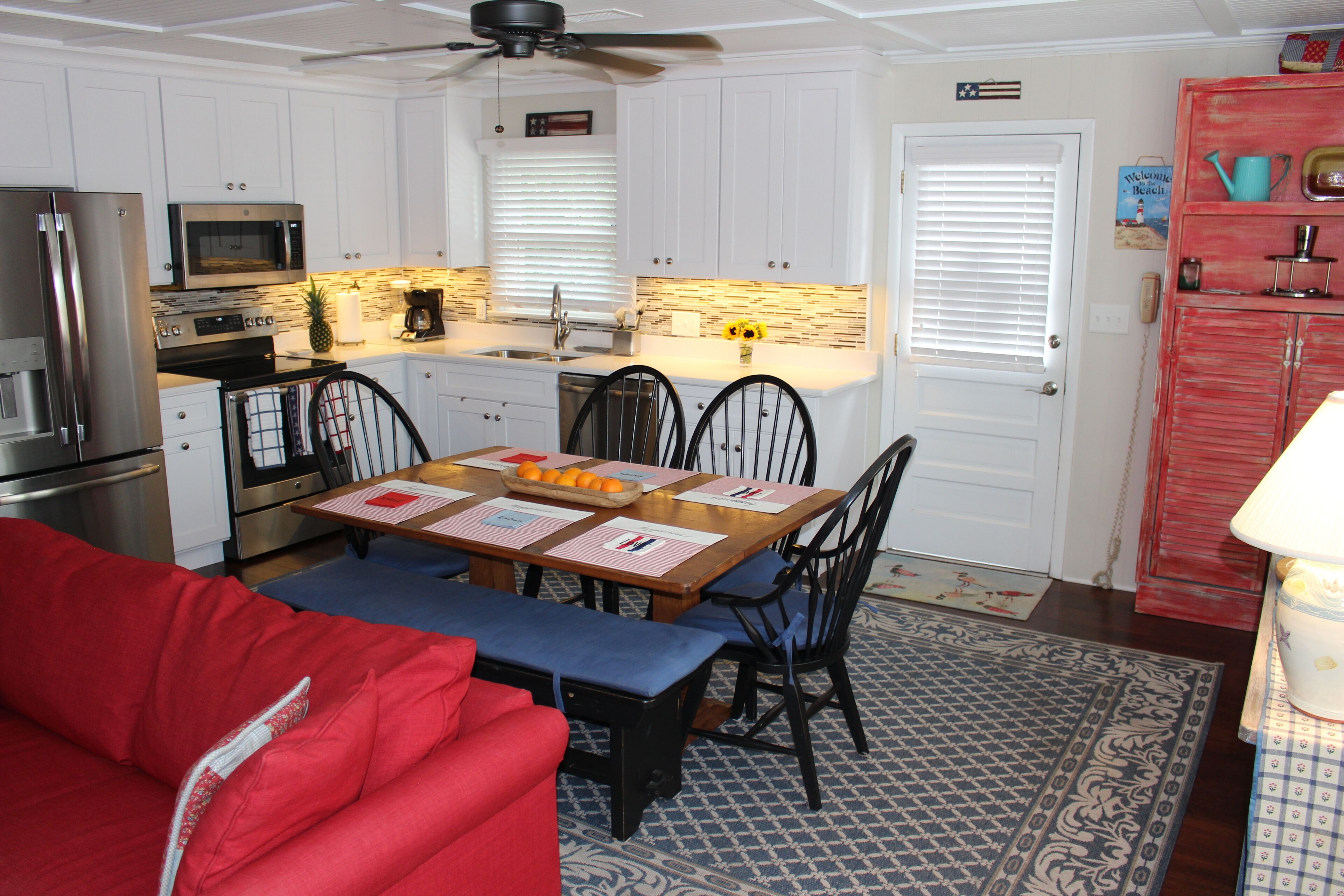 A compact kitchen with white cabinets, a microwave, stove, and a red refrigerator.
