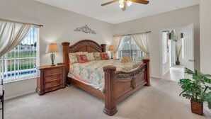 A bedroom with a wooden bed, two bedside tables with lamps, a ceiling fan, and a view of a tennis court through the window. - 4 bedrooms home with private pool- 15 min from Disney (Davenport)