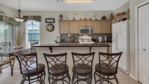 A kitchen with a central island, a microwave, a refrigerator, and a dining area with chairs. - 4 bedrooms home with private pool- 15 min from Disney (Davenport)