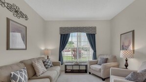 A living room with a beige sofa, two armchairs, a coffee table, and a window with curtains. - 4 bedrooms home with private pool- 15 min from Disney (Davenport)