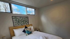 A neatly made bed with a white quilt, a wooden headboard, and a bedside table with a lamp. - Blencathra Coastal Spa Getaway (Currie King Island)