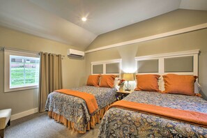 A bedroom with two beds, beige walls, a window with curtains, and an air conditioning unit. - 2 Mi to Branson Strip: Cozy Cottage w/ Fire Pit! (Branson)