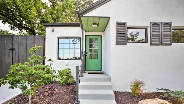 A modern house with a green door, a small front yard with mulch, a wooden fence, and a rock. - 2 Mi to Branson Strip: Cozy Cottage w/ Fire Pit! (Branson)