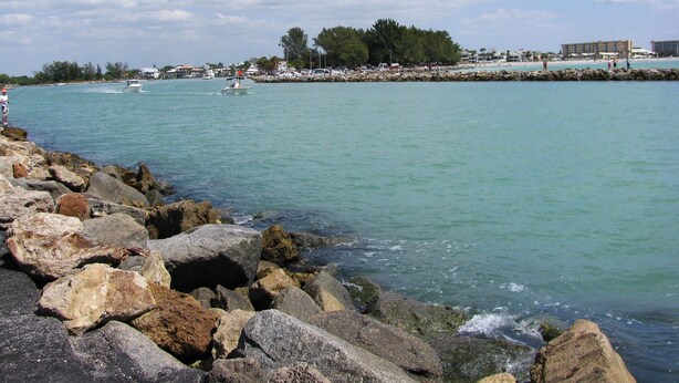 A coastal scene with rocky shoreline, calm water, and distant buildings.