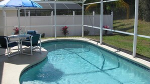A swimming pool with a white fence, a table with chairs, and an umbrella.