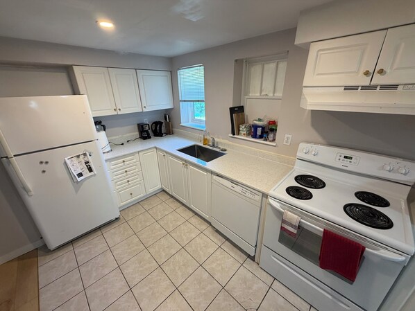 A kitchen with white cabinets, a white refrigerator, a sink, a stove, and a window with blinds.