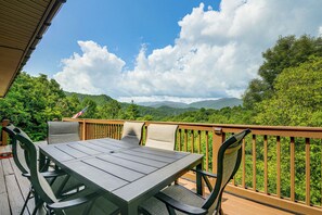 Eine Terrasse mit Tisch und Stühlen, mit Blick auf eine bewaldete Landschaft und Berge in der Ferne.