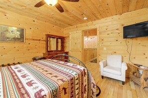 Ein Zimmer in einer Holzhütte mit einem Bett, einem Sessel, einem Fernseher und einem Deckenventilator.
