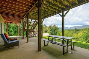 A covered outdoor area with a picnic table and chairs, a staircase, and a view of a lush landscape. - Hot Tub & Mtn Views: Beautiful Bryson City Home (Bryson City)