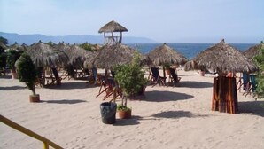 A beach with thatched umbrellas and lounge chairs, a clear sky, and a distant view of the sea. - Playa Bonita Casa de Risa located on Los Muerto Beach  2BD Condo for rent in Los (Puerto Vallarta)