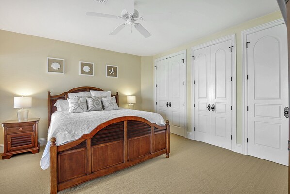 A bedroom with a wooden bed, a nightstand, a ceiling fan, and a set of white doors.