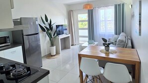 A modern kitchen with a refrigerator, microwave, and gas stove. There is a dining area with a wooden table and chairs, and a TV on a stand.