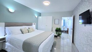 A modern hotel room with a large bed, a TV, and a bathroom visible through an open door.