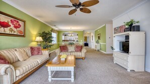 A spacious living room with a sofa, coffee table, and a television cabinet. - 325 River Crossing - Barefoot Resort Rentals (North Myrtle Beach)