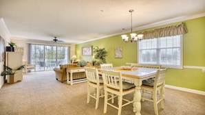 A dining area with a table and chairs, a ceiling fan, and a view through a glass door to an outdoor patio. - 325 River Crossing - Barefoot Resort Rentals (North Myrtle Beach)