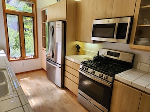 A kitchen with wooden cabinets, stainless steel appliances, a window, and a tiled backsplash. - Snowcreek Resort Vacation Rental 934 (Mammoth Lakes)