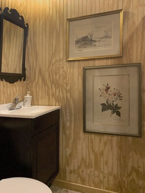 A bathroom with wooden paneling, a sink with a mirror, and two framed pictures on the wall. - Charming & Cozy Mountain View Cottage with River Hi-spd-wifi / pets welcome (Thornton)