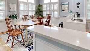 Una cocina moderna con una isla central, armarios blancos y un comedor con sillas de madera.