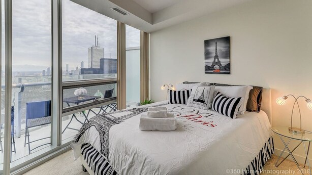 A modern bedroom with a large bed, a city view, and a framed picture of the Eiffel Tower.
