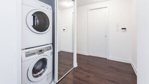 Une buanderie avec deux machines à laver et deux sèche-linge superposés, un plancher en bois et une porte blanche à l’arrière-plan.
