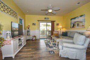Relax in this inviting living room with a sofa, TV, and ceiling fan, plus a sliding door to a balcony.