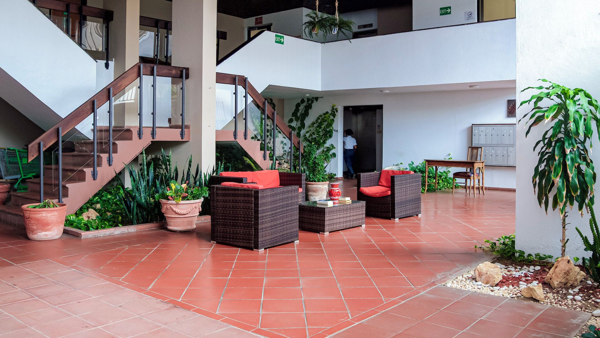 Un espace intérieur spacieux avec un escalier, des meubles en osier, des plantes en pot et un sol carrelé.