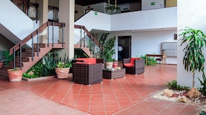 A spacious indoor area with a staircase, wicker furniture, potted plants, and a tiled floor.