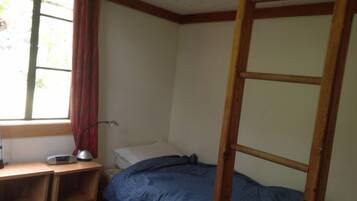 A small, single-bed room with a wooden bunk bed, a desk with a lamp, and a window with curtains.