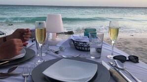 A table set for two with wine glasses, a lamp, and a view of the ocean. - Private chef,46 sec to WATER, Pool side massage, UTV (Eagle Beach)