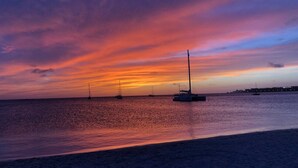 A beach scene with a sunset, calm sea, and sailboats. - Private chef,46 sec to WATER, Pool side massage, UTV (Eagle Beach)