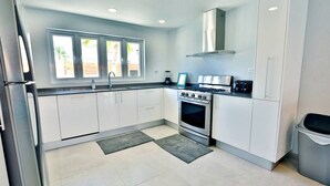 A modern kitchen with white cabinets, stainless steel appliances, a gas stove, and a large window with a view of palm trees. - Private chef,46 sec to WATER, Pool side massage, UTV (Eagle Beach)