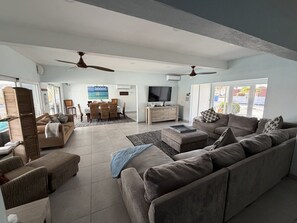 Een ruime woonkamer met een grote bank, een televisie en een eethoek met een tafel en stoelen.