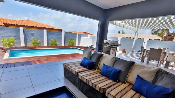 A modern outdoor living area with a pool, a sofa with cushions, and a grill. - Private chef,46 sec to WATER, Pool side massage, UTV (Eagle Beach)