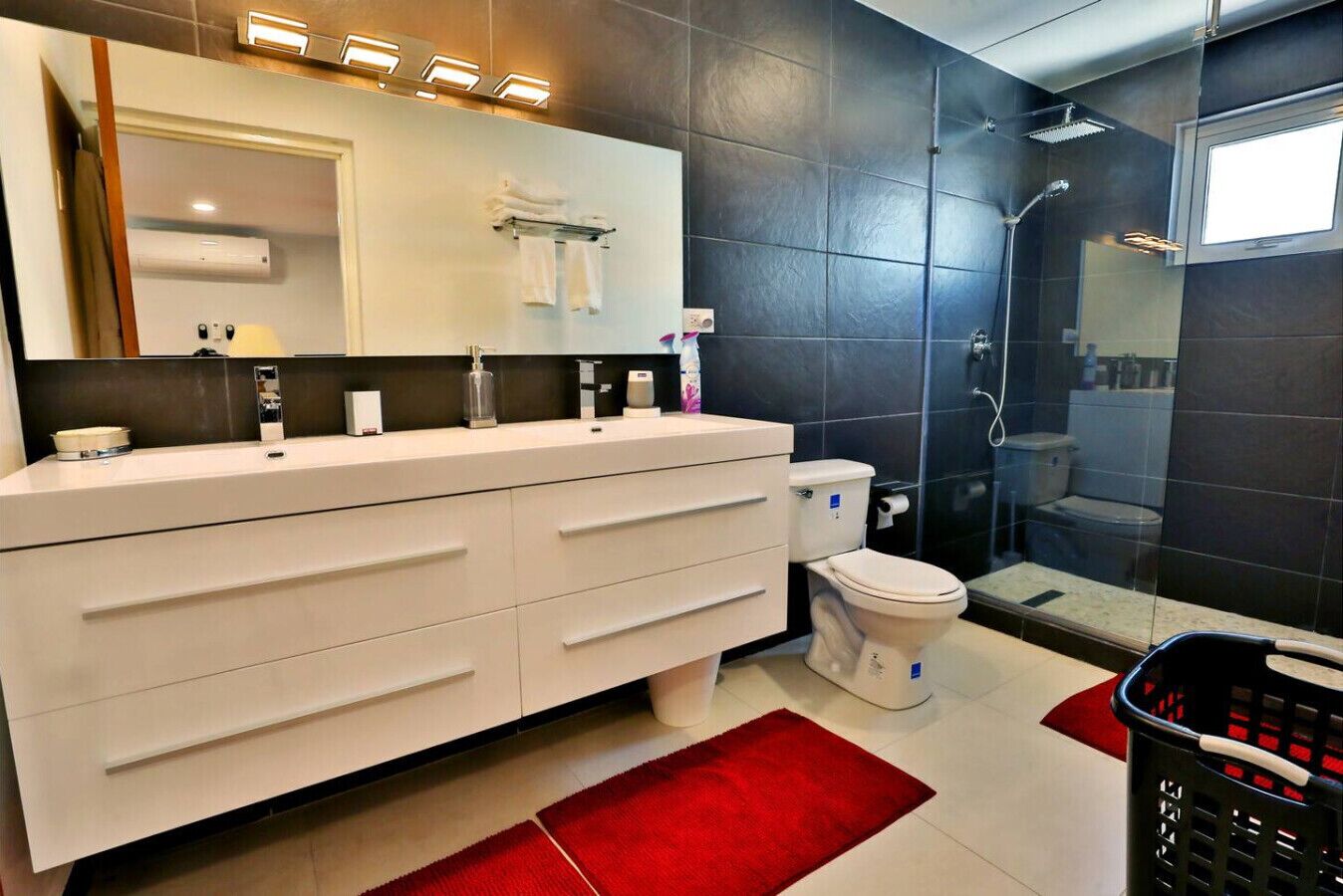 Une salle de bain moderne avec un meuble-lavabo blanc, des toilettes, un espace douche et un tapis rouge.